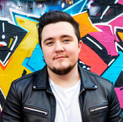 a photo of Grayson smiling in front of a graffiti wall